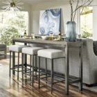 Industrial-style console table with a natural wood top, black metal frame, and three upholstered stools in ivory fabric.