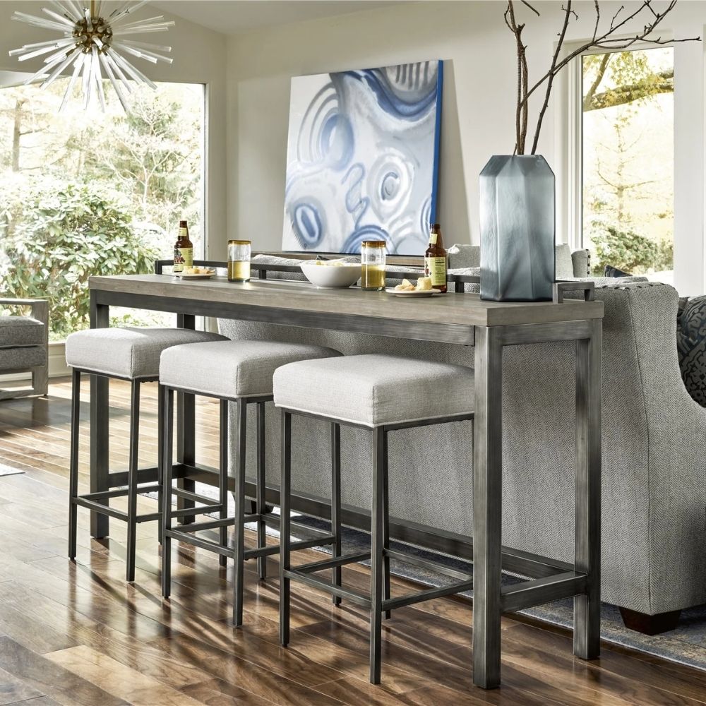 Industrial-style console table with a natural wood top, black metal frame, and three upholstered stools in ivory fabric.