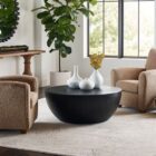 Round black coffee table with a smooth, matte finish and softly curved base in a minimalist drum silhouette