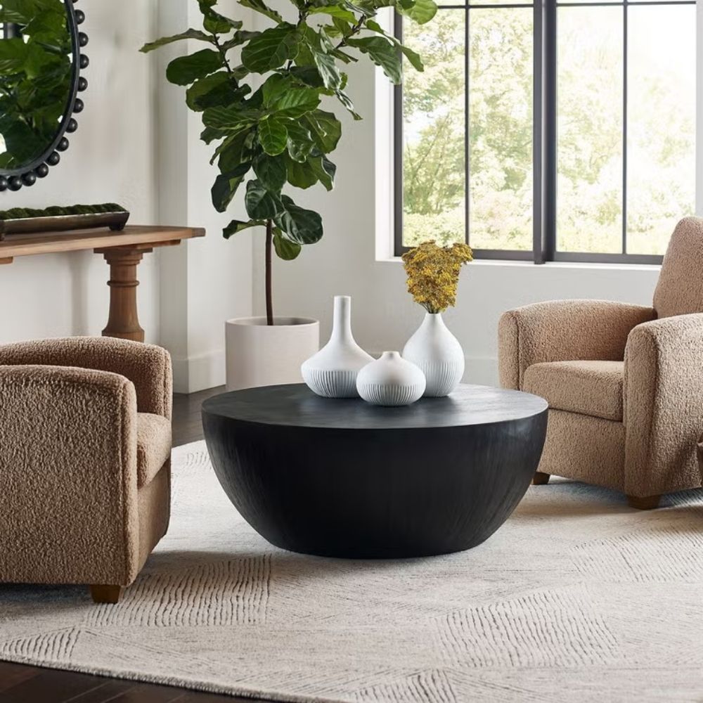 Round black coffee table with a smooth, matte finish and softly curved base in a minimalist drum silhouette