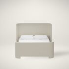 The Tilburg Bed featuring a high, fully upholstered headboard and footboard in a soft neutral fabric with a clean, curved silhouette.