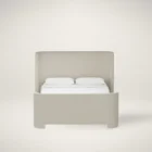 The Tilburg Bed featuring a high, fully upholstered headboard and footboard in a soft neutral fabric with a clean, curved silhouette.