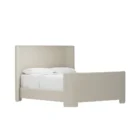 The Tilburg Bed featuring a high, fully upholstered headboard and footboard in a soft neutral fabric with a clean, curved silhouette.