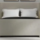 The Tilburg Bed featuring a high, fully upholstered headboard and footboard in a soft neutral fabric with a clean, curved silhouette.