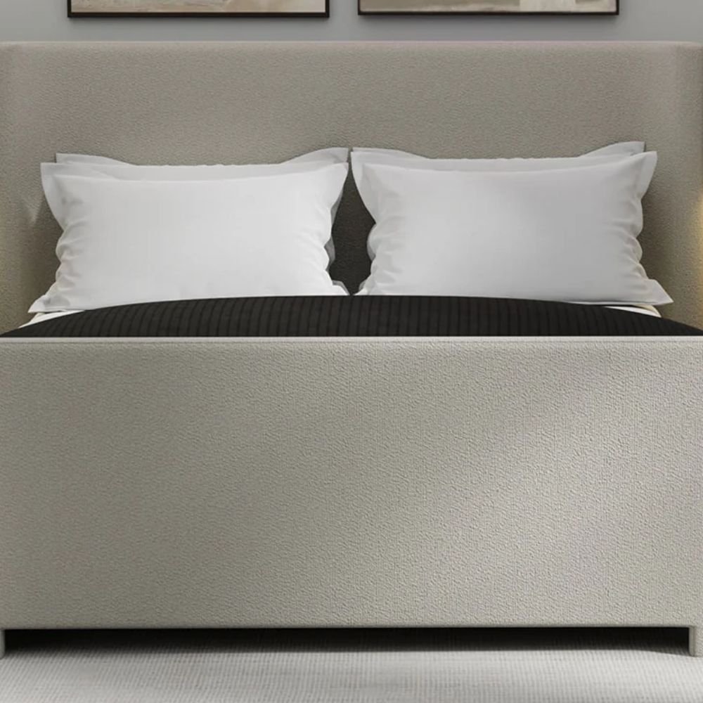 The Tilburg Bed featuring a high, fully upholstered headboard and footboard in a soft neutral fabric with a clean, curved silhouette.