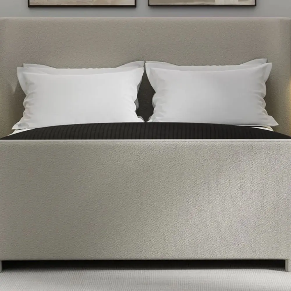 The Tilburg Bed featuring a high, fully upholstered headboard and footboard in a soft neutral fabric with a clean, curved silhouette.