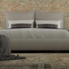 Upholstered Bed with Double-Cushion Headboard and Rounded Base, Dressed in Neutral Bedding.