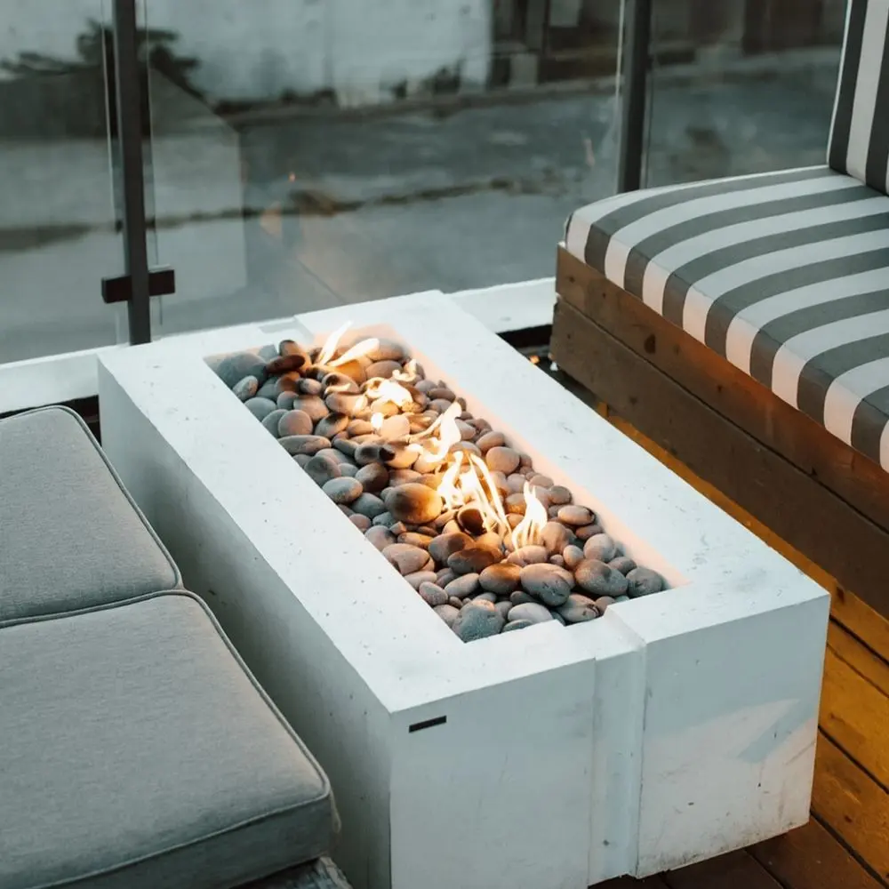 A sleek rectangular Dekko Avera 48 firepit in a minimalist concrete finish, showcasing a linear flame bed with lava rock fill.