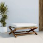 Outdoor teak stool with white cushion and slatted wood frame.