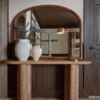 A sleek oval-shaped Renwell Kindra Mirror with a thin, minimal metal frame in a warm brass finish, mounted on a light-toned wall.