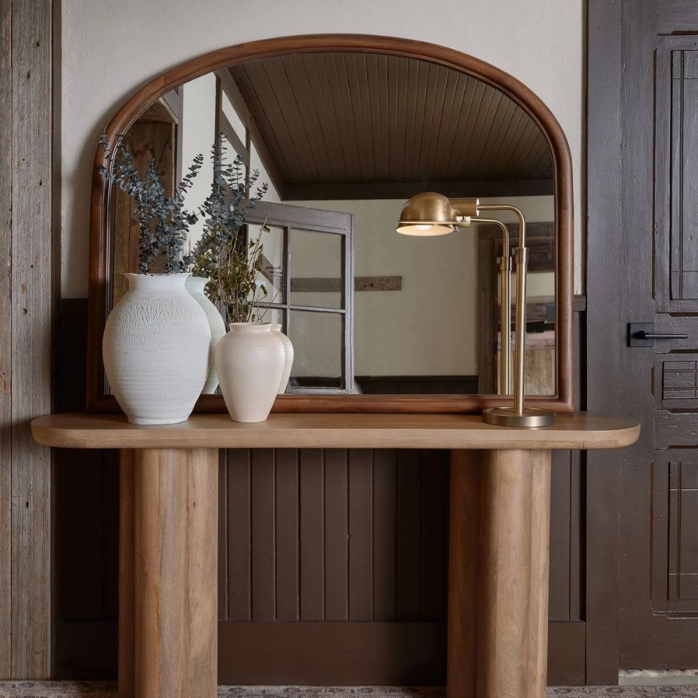 A sleek oval-shaped Renwell Kindra Mirror with a thin, minimal metal frame in a warm brass finish, mounted on a light-toned wall.