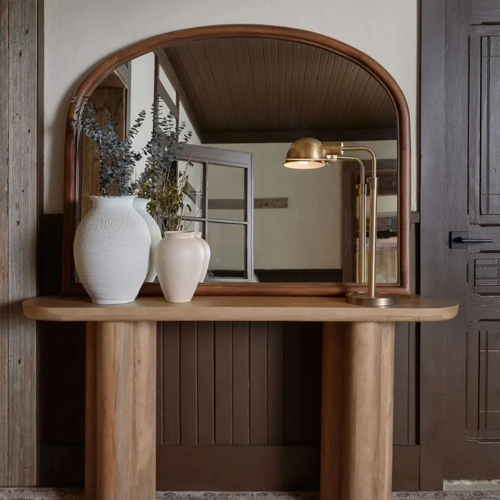 A sleek oval-shaped Renwell Kindra Mirror with a thin, minimal metal frame in a warm brass finish, mounted on a light-toned wall.