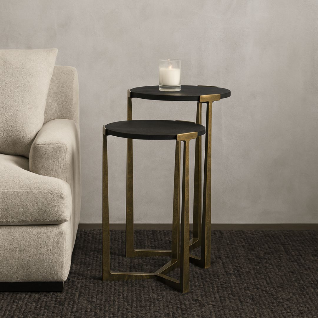 Pair of round nesting accent tables with charcoal wood tops and antique brass metal frames.