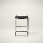 Minimalist counter-height stool with dark woven leather seat and slender black metal frame.