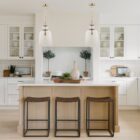 Tall clear glass pendant light with gold metal hardware and a single exposed bulb, suspended from a matching gold chain.