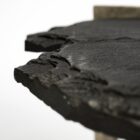 Irregular black stone coffee table with a jagged, organic edge and industrial hammered metal base.