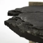 Irregular black stone coffee table with a jagged, organic edge and industrial hammered metal base.