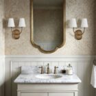 Double-arm wall sconce with antique brass finish and white fabric shades.