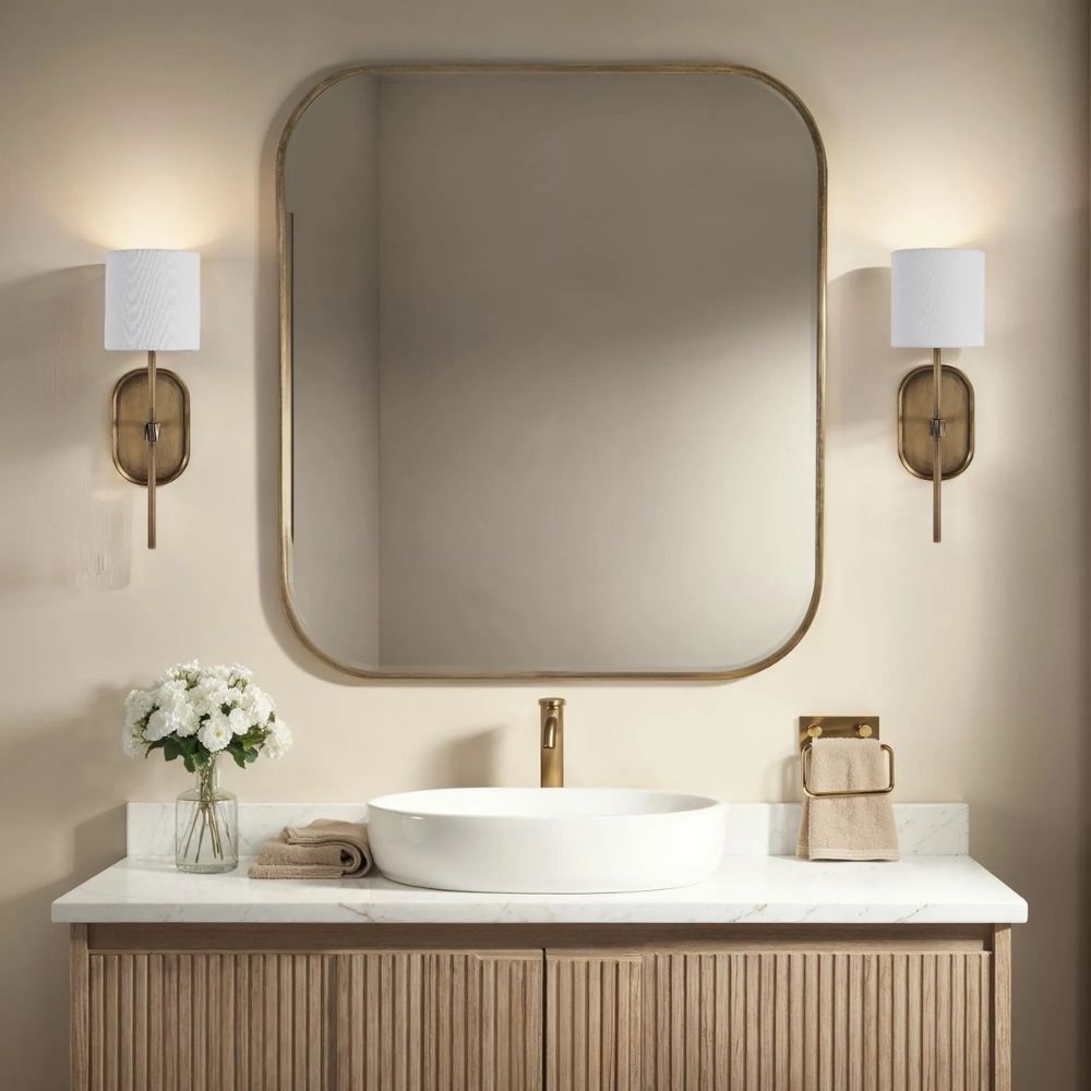 Brushed brass wall sconce with a white cylindrical fabric shade and elongated backplate.
