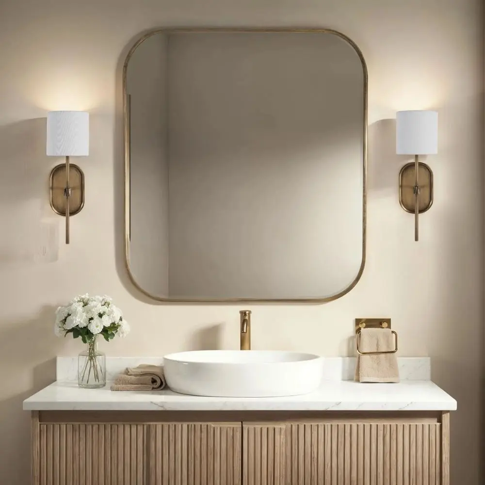 Brushed brass wall sconce with a white cylindrical fabric shade and elongated backplate.