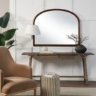 A sleek oval-shaped Renwell Kindra Mirror with a thin, minimal metal frame in a warm brass finish, mounted on a light-toned wall.