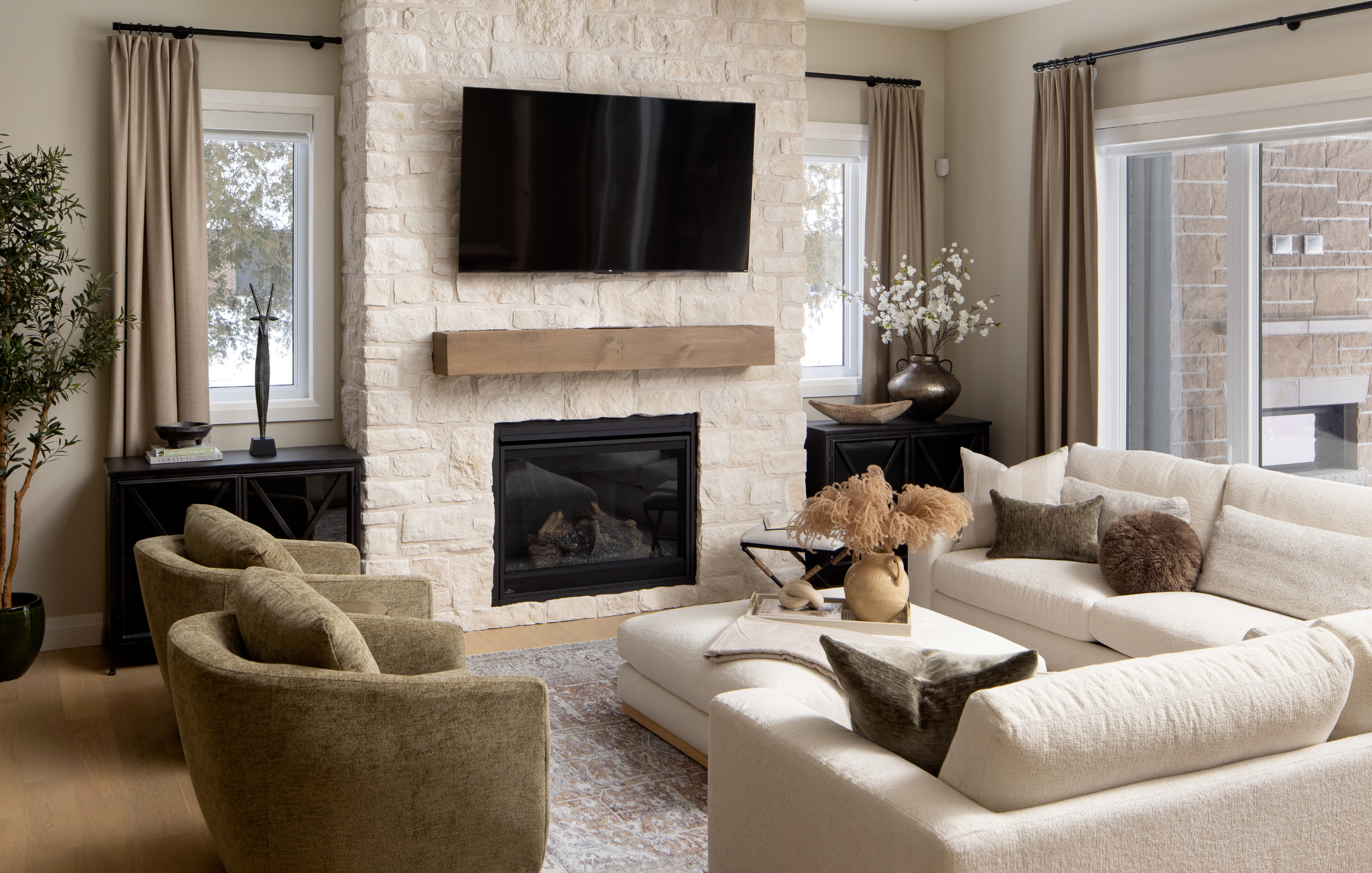 Elegant living space with neutral sectional, green accent chairs, and stone fireplace.