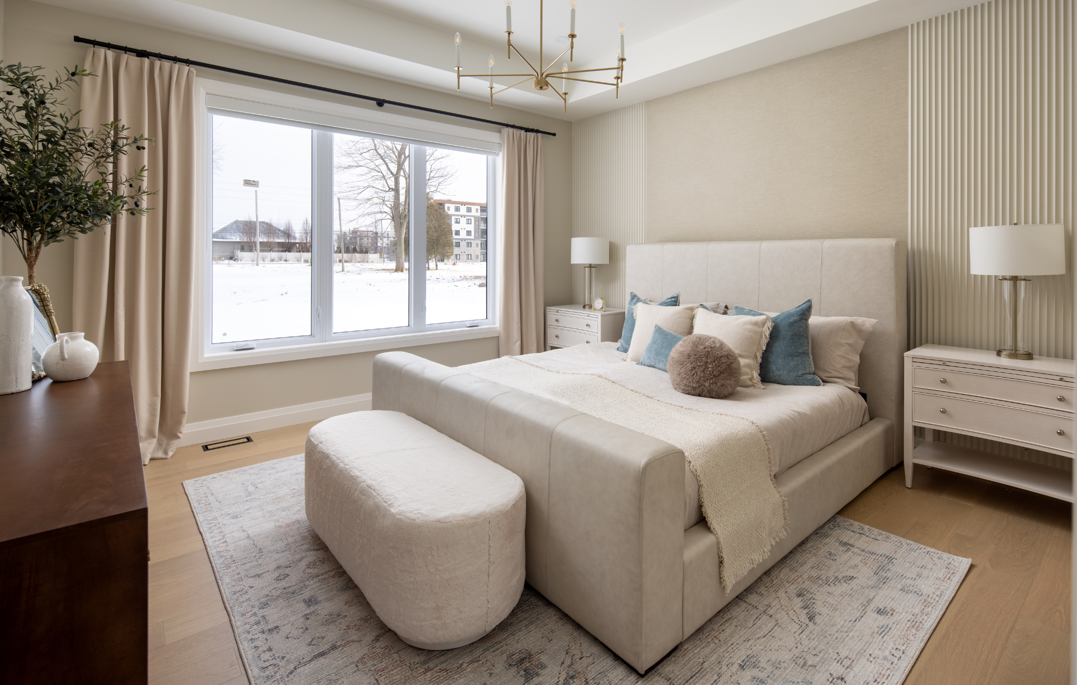 Elegant bedroom with upholstered bed, layered neutral bedding, and large window with natural light.