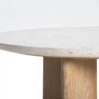 Round coffee table with a white stone top and sculptural blonde wood base in an intersecting design.