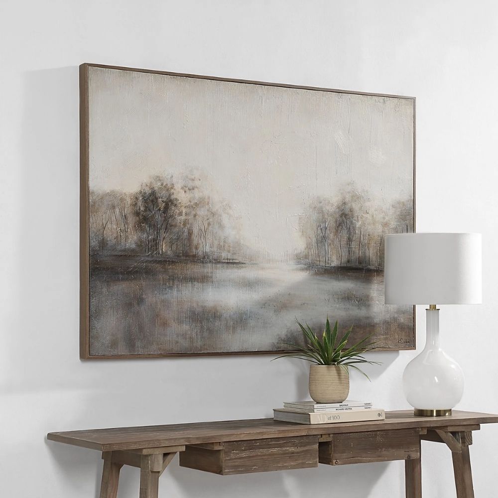 A serene landscape wall art piece featuring soft neutral tones of grey, beige, and white with a misty treeline reflected on calm water, framed in a slim border.