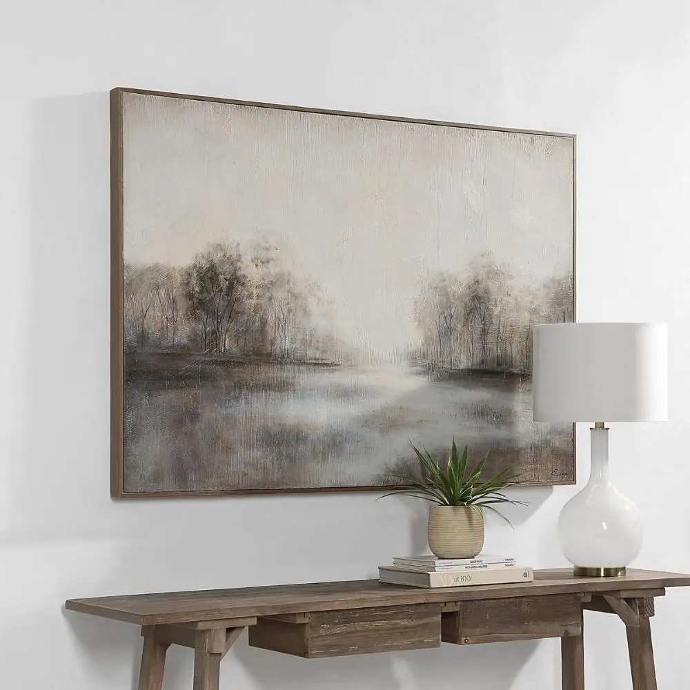 A serene landscape wall art piece featuring soft neutral tones of grey, beige, and white with a misty treeline reflected on calm water, framed in a slim border.