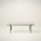A minimalist upholstered bench in ivory boucle fabric with slim antique brass-finished tapered legs.
