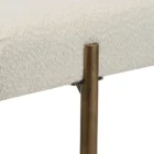 A minimalist upholstered bench in ivory boucle fabric with slim antique brass-finished tapered legs.