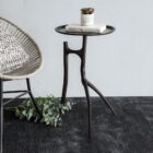 A sculptural black metal side table with a round top and organic tripod-style base featuring asymmetrical, branch-like legs.