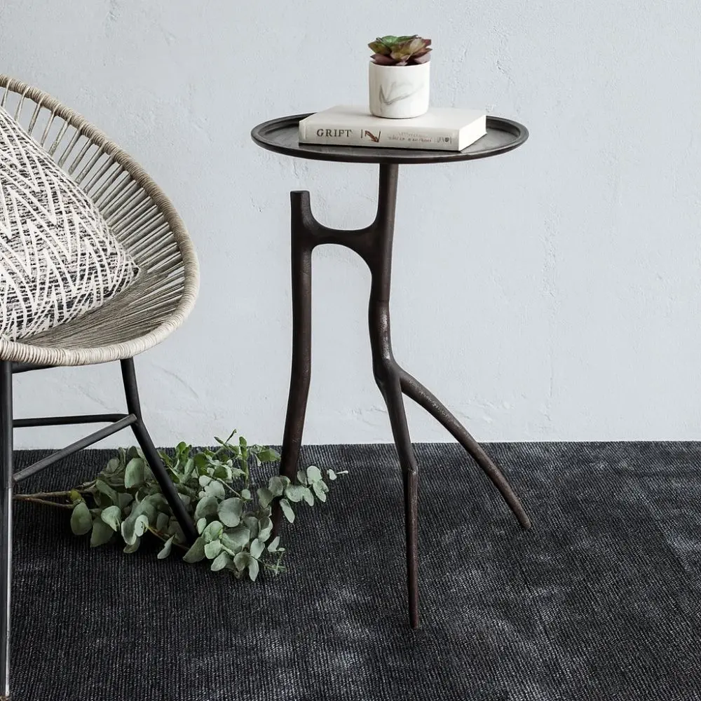 A sculptural black metal side table with a round top and organic tripod-style base featuring asymmetrical, branch-like legs.