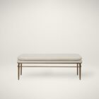A modern upholstered bench with a slim ivory cushion and sleek antique brass-finished metal frame with tapered legs