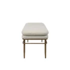 A modern upholstered bench with a slim ivory cushion and sleek antique brass-finished metal frame with tapered legs