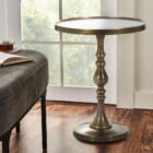 A round brass side table with a sculpted pedestal base and raised edge, featuring an antique finish and elegant silhouette.