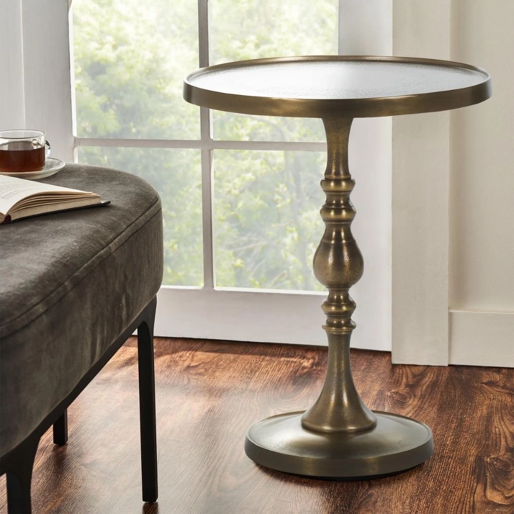 A round brass side table with a sculpted pedestal base and raised edge, featuring an antique finish and elegant silhouette.