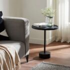 A modern black side table with a round top, slim central support, and cylindrical base in a minimalist design.