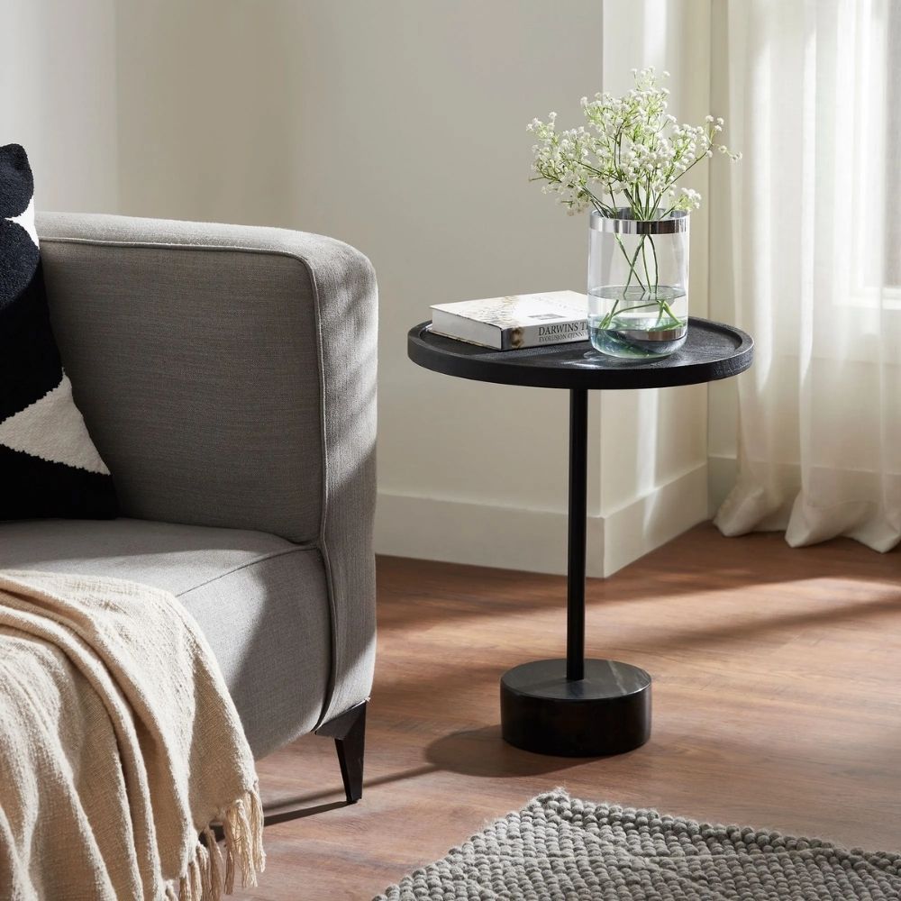 A modern black side table with a round top, slim central support, and cylindrical base in a minimalist design.