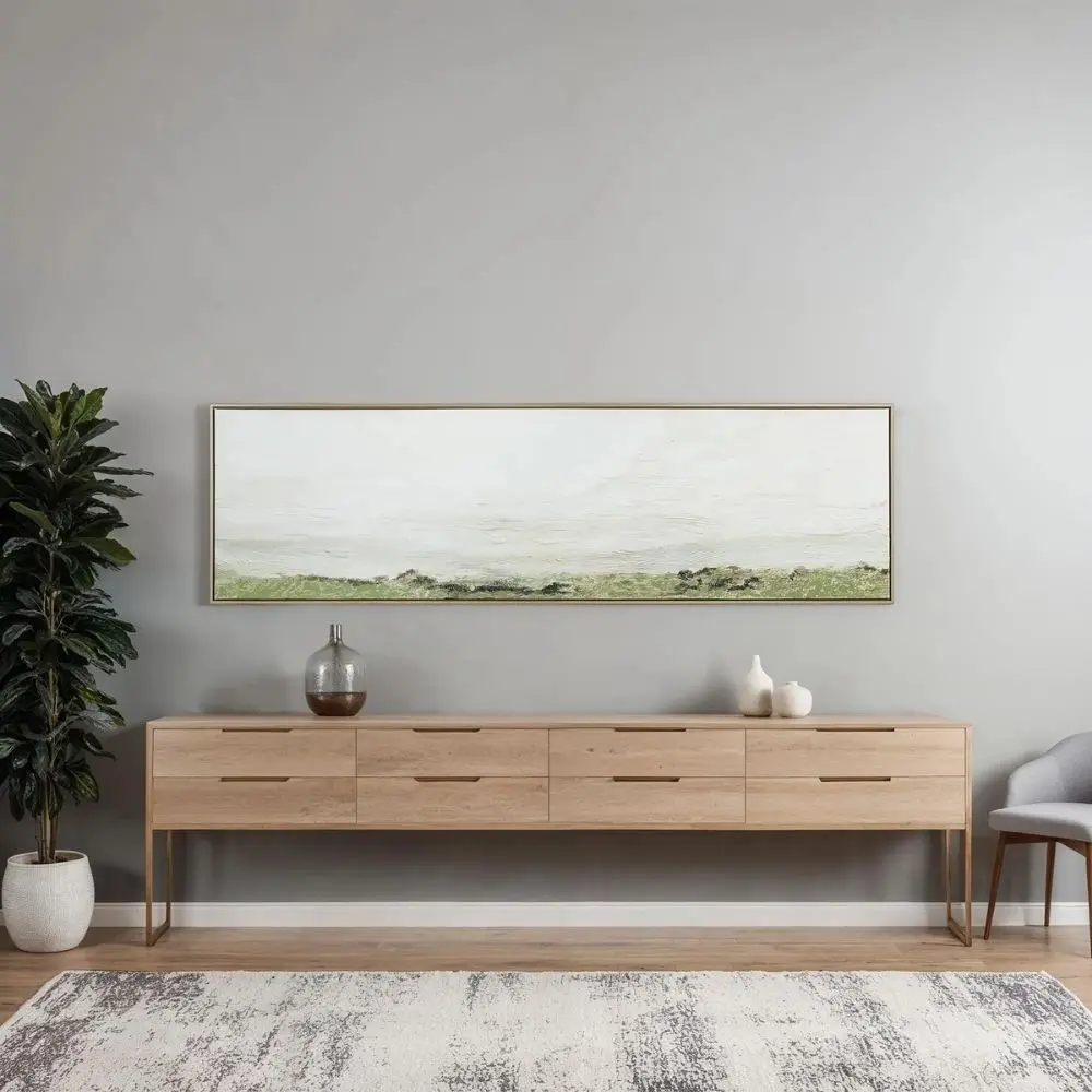 A panoramic landscape wall art piece featuring soft textured strokes of green fields beneath a wide expanse of pale sky, framed in a slim border.