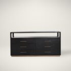 A modern black six-drawer dresser with slim brass handles, open top shelf, and a brass base accent.