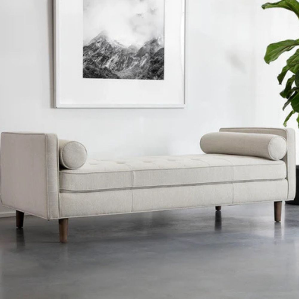 Contemporary upholstered bench with tufted seat, bolster cushions, and wooden legs in soft light fabric.