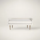 White upholstered bench with slim curved backrest and tapered gold-finished legs.