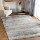 Modern distressed rug in layered blue, taupe, and grey tones with an abstract weathered finish.