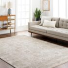 Neutral woven rug with a subtle distressed floral medallion pattern in beige and ivory tones.