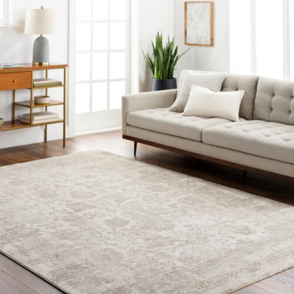 Neutral woven rug with a subtle distressed floral medallion pattern in beige and ivory tones.