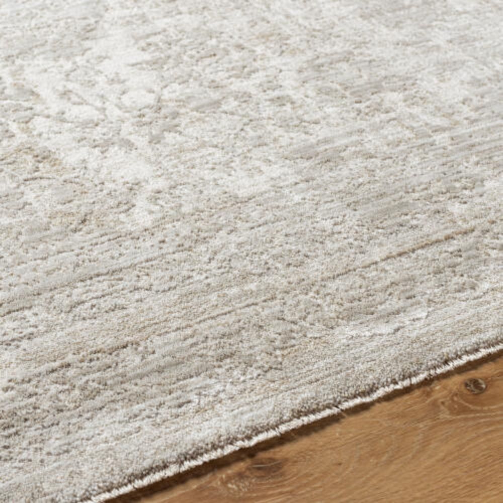 Neutral woven rug with a subtle distressed floral medallion pattern in beige and ivory tones.