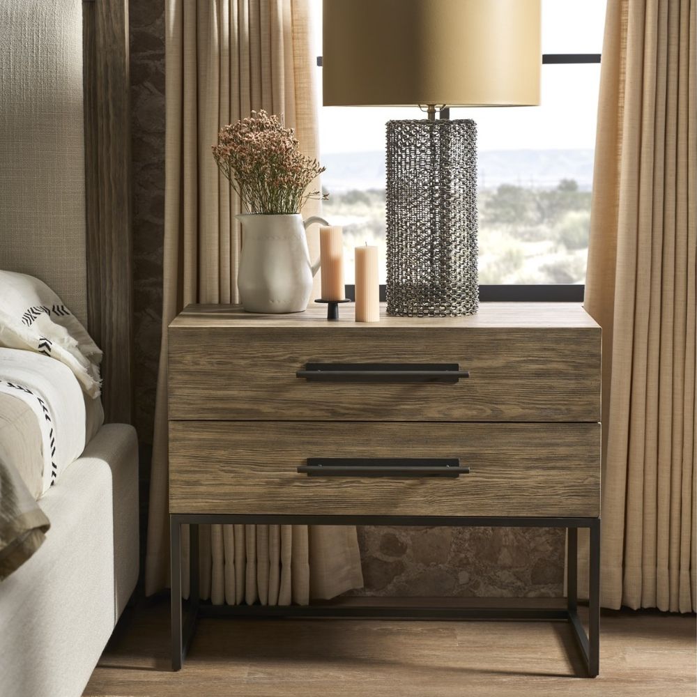 A modern nightstand in a light natural wood finish with two drawers, oversized black metal handles, and an open metal base frame.