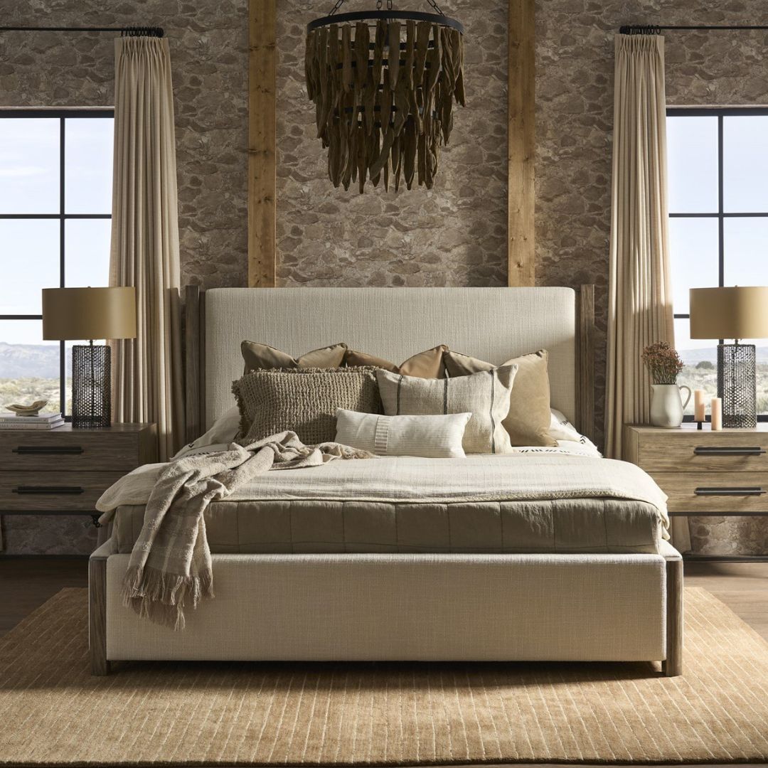 A contemporary upholstered bed in soft beige fabric with a tall padded headboard and natural wood trim accents on the corners and legs.